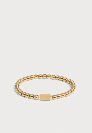 Bracelet en perles dorées avec fermoir rectangulaire présentant un design gravé subtil, montré sur un fond clair uni.