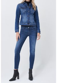 Denim jacket in medium blue with four pockets, button front, and fitted design. Paired with skinny jeans and black ankle boots.