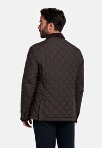 Gev quilted bruin jack met een gestructureerde afwerking, met een kraag en een accentdetail aan de zijkant. De mouwen zijn licht getailleerd, wat een gestructureerde vorm biedt.