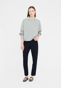 Sweatshirt gris avec des manches retroussées, superposé à une chemise à col à carreaux bleus. Associé à un pantalon marine foncé et des ballerines noires.