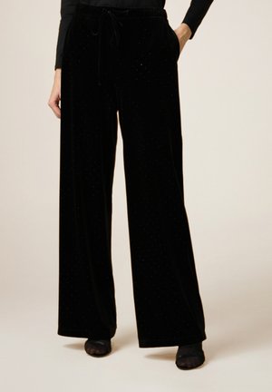 Pantalon large en velours noir avec une taille à cordon et des embellissements subtils, conçu pour le confort et une coupe décontractée.