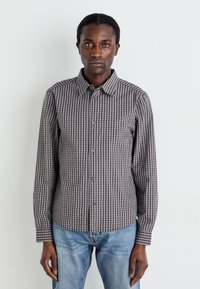 Button-up shirt in checkered pattern, featuring brown and white colors. Long sleeves, collar, and regular fit. Paired with blue denim jeans.