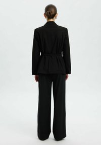 Blazer noir ajusté avec une taille cintrée, doté de manches longues et d'un dos fluide. Assorti à un pantalon noir à larges jambes.