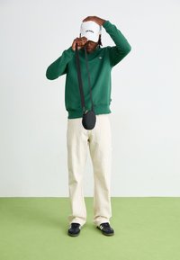 Green sweatshirt, beige striped pants, black circular crossbody bag, black sneakers with white stripes, and a white cap. Simple design and casual.