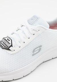 Baskets blanches antidérapantes avec un dessus en tissu texturé, semelle intérieure en mousse à mémoire de forme et un accent de logo brillant sur le côté. Design à lacets.