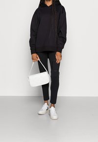 Czarna bluza z kapturem, dopasowane czarne legginsy, biała pikowana torebka oraz białe trampki z czarnymi akcentami. Prosty i nowoczesny design.