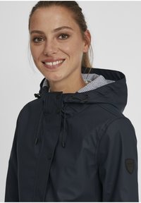 Veste imperméable bleu marine avec capuche, dotée d'une doublure intérieure rayée, de cordons de serrage réglables et d'un logo sur le côté.