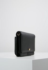 Bolso de mano de piel negra con acabado texturizado, detalles de metal dorado, diseño plegado y logotipo en la parte frontal. Forma compacta y estructurada.
