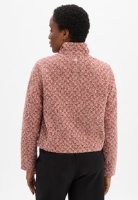 Kürzer geschnittene Jacke in Rot und Pink mit gepunktetem Muster, hohem Kragen, strukturiertem Stoff und kleinem Logo am Nacken. Schlichtes, tailliertes Design.