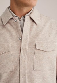 Lichtbeige wollen blend shirtjacket met een kraag, drukknoopsluiting, twee borstzakken en een subtiele textuur. Gestreept shirt zichtbaar eronder.
