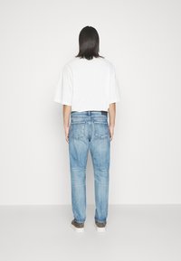 Lichtblauwe spijkerbroek met een rechte snit, met achterzakken en een zwart label op de tailleband. Gecombineerd met een losse witte T-shirt en grijze schoenen.