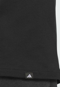 Černé bavlněné tričko s prošitým lemem a štítkem s logem Adidas v levém dolním rohu. Hladká textura a klasický střih.