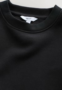 Zwarte crewneck sweatshirt gemaakt van zacht materiaal. Voorzien van een ribbelboord en een label met "NEXT". Soepele textuur zonder patronen.
