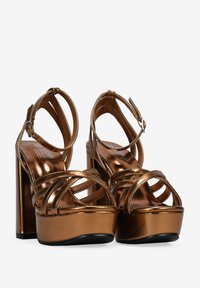 Sandales plateforme en bronze avec un talon haut épais. Le design à lanières présente de fines lanières métalliques et une finition lisse. Semelle noire.