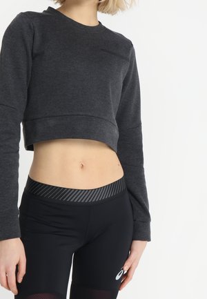 Osoba ubrana w ciemnoszarą krótką bluzę i czarne sportowe legginsy z wysokim stanem i paskiem w paski.