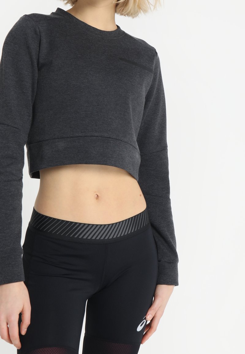 Personne portant un sweat-shirt court gris foncé et des leggings de sport noirs taille haute avec une ceinture rayée.