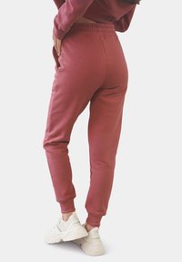 Bordeauxfarbene Jogginghose aus weichem Stoff, mit elastischem Bund, seitlichen Taschen und schmal zulaufenden Beinen, kombiniert mit weißen Sneakers.