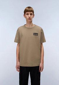 Kaki katoenen T-shirt met korte mouwen, ronde hals en een klein zwart logo op de linkerborst. Platte, gladde textuur. Casual pasvorm.