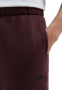 Bordeaux sweatpants gemaakt van gestructureerde fleece met een zichtbare zak en een zwart Vans-logo op het onderbeen. Elastische tailleband.