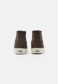 Sapatilhas altas em corduroy castanho com sola de borracha branca e logótipo na parte de trás. Apresentam uma textura em cordas e um design de bico arredondado.