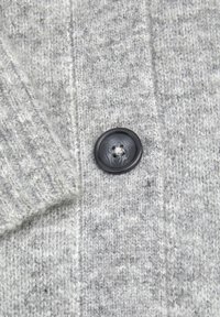 Tissu en tricot gris avec un motif texturé et un bouton noir proéminent présentant un design en spirale.