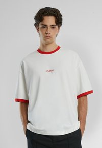 T-shirt bianca a maniche corte con colletto e polsini rossi, con il testo ricamato "Proibito" sul davanti. Tessuto di cotone liscio.