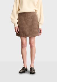 Mini falda marrón texturizada con un diseño ajustado, combinada con un suéter de canalé color crema y mocasines oscuros. La tela presenta un patrón sutil.