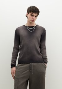 Grijze gradient geribbelde trui met lange mouwen, met een ronde hals. Gecombineerd met losse, grijze broek met trekkoord. Zilveren kettingen.