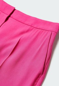 Pantalon rose vif avec taille haute, pli devant et poches latérales sur un fond uni clair.