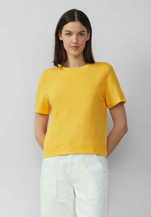 Geel T-shirt met korte mouwen, gemaakt van katoen met een ronde halslijn, met een ontspannen pasvorm en een gladde textuur. Gecombineerd met witte broek.