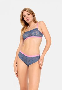 Kant bralette en bijpassende slip in donkerblauw met roze rand. Voorzien van delicate bloemenpatronen en een geschulpte rand. Verstelbare bandjes.