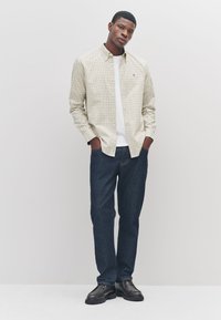 Checkered beige and green shirt paired with a white t-shirt, dark blue jeans, and black shoes. Features a button-down collar and pockets.