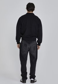 Black sweatshirt with long sleeves, paired with dark denim jeans. The fit is relaxed, and the sweatshirt has a crew neck design.