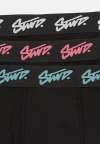 Czarny, elastyczny materiał z trzema elastycznymi paskami w talii. Paski w talii mają napis "Stand" w kolorach białym, różowym i niebieskim na czarnym tle.