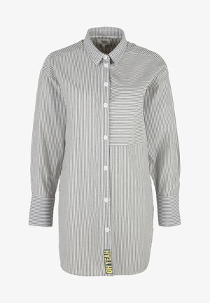 Camicia a maniche lunghe con bottoni, righe verticali, tasca a contrasto, polsini ampi e scritta "OH YEAH" sull'orlo inferiore.