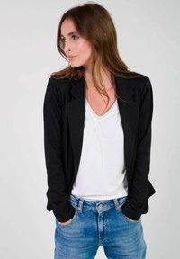 Svart kavaj med skräddarsydd passform, tillverkad av mjukt tyg, bärs över en vit V-ringad skjorta och kombineras med ljusblå denimjeans.