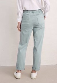 Pantalon en denim bleu clair avec une taille élastique, deux poches arrière et des poignets retroussés, associé à des chaussures blanches à enfiler. Conception simple et coupe décontractée.