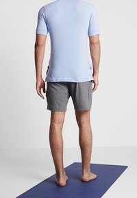 Camiseta atlética de manga corta azul claro combinada con pantalones cortos gris, ambos hechos de un tejido transpirable, posicionados sobre una esterilla de yoga.