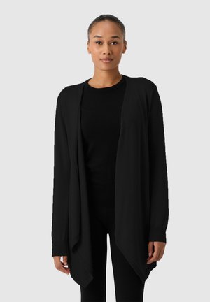 Czarny kardigan otwarty z długimi rękawami, miękka faktura i asymetryczny dół, nałożony na czarny top.