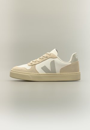 Baskets basses à lacets en blanc et beige avec une semelle épaisse et un grand logo "V" sur le côté.