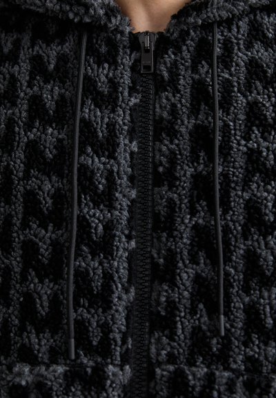 Black fleece hoodie featuring a textured, looped surface, zip closure, and drawstring accents along the hood.