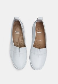 Witte lederen instappers met een ronde neus, geperforeerde binnenzool en een lus aan de achterkant voor gemakkelijk aantrekken. Heeft subtiele stiksels.
