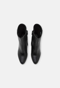 Botines de cuero negro con diseño de puntera afilada, textura suave y cierre de cremallera lateral, vistos desde arriba.