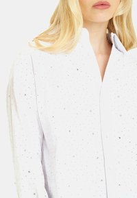 Camicia bianca con bottoni caratterizzata da numerosi piccoli paillettes luccicanti distribuiti uniformemente sul tessuto, creando un effetto texture scintillante.