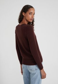 Pull en maille bordeaux avec un col rond, des manches longues et des bordures côtelées. Texture douce et design ajusté. Associé à un jean bleu clair.