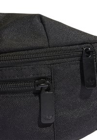 Sac à taille en tissu noir texturé avec deux compartiments zippés, avec des tirettes de zip noires embossées d'un logo trèfle.