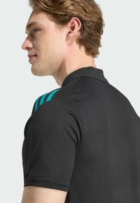 Polo noir avec un tissu texturé, rehaussé de rayures teal sur l'épaule gauche ; design ajusté avec un col classique.