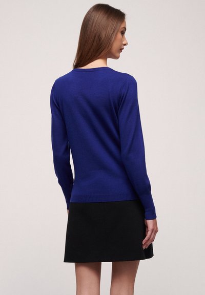 Königsblauer Strickpullover mit langen Ärmeln, schmaler Passform und geripptem Saum, kombiniert mit einem schwarzen Rock. Glatte Textur ohne auffällige Muster.