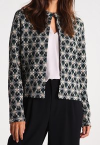 Knitted jacket featuring a geometric pattern in green, white, and gray. It has long sleeves and a round neckline with a short front opening.