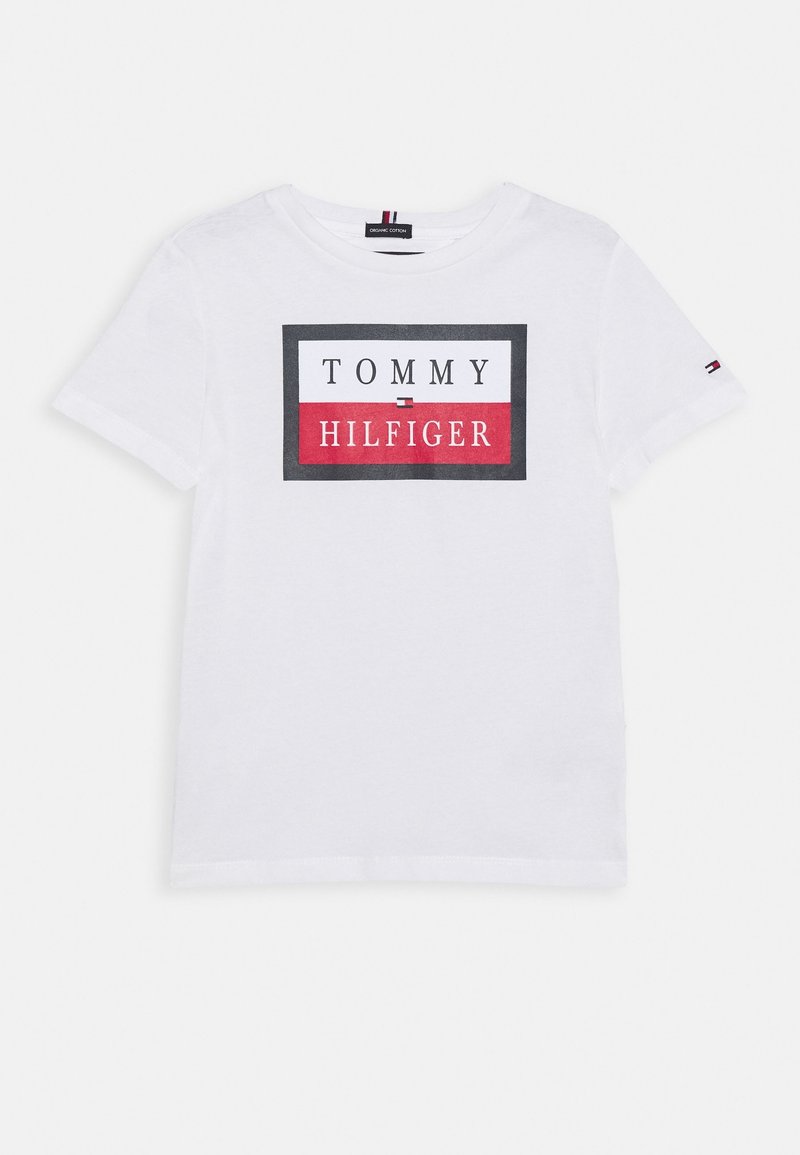 Bílý bavlněný tričko s obdélníkovou grafikou a textem "TOMMY HILFIGER" v černé, červené a bílé barvě. Krátké rukávy, kulatý výstřih.